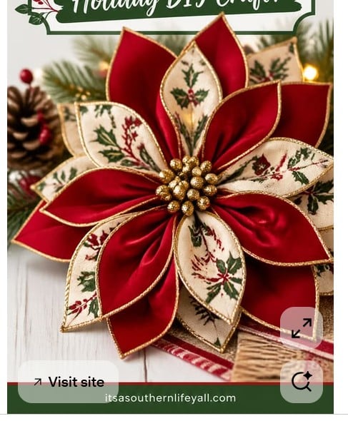 A festive handmade ornament shaped like a poinsettia flower, with alternating red satin and cream fabric petals featuring holly designs, gold trim, and a cluster of gold beads in the center. Pine branches and pinecones in the background.