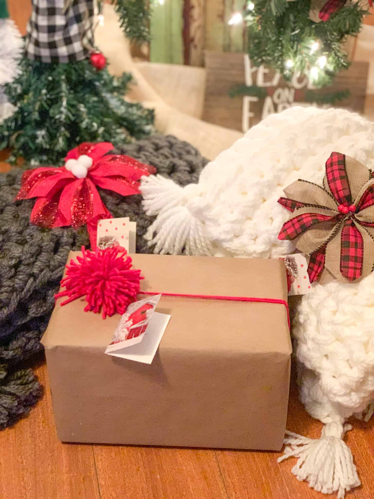 Picture from Christmas showing simply wrapped gift with yarn and pom with hand crocheted blankets adorned with ribbon poinsettias. 