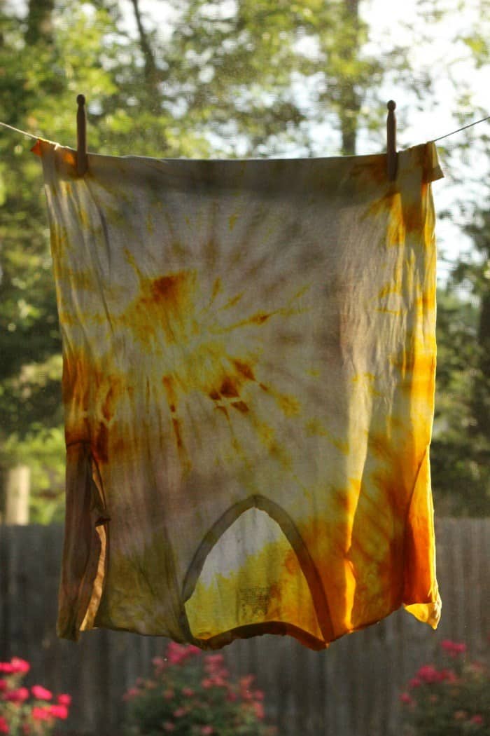 Turmeric tie dyed t-shirt hanging upside down from a clothesline outdoors.