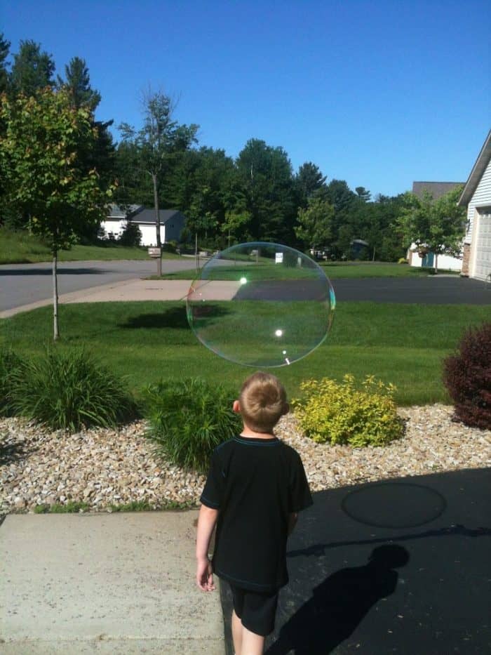 Young boy in yard with gigantic bubble floating by him.