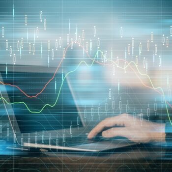 A person types on a laptop with transparent graphs and financial data overlays, symbolizing data analysis, stock market trends, or financial trading in a digital environment.