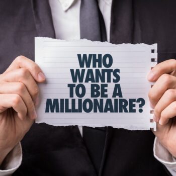 A person in a suit holds a piece of torn paper with the text WHO WANTS TO BE A MILLIONAIRE? printed in bold letters.