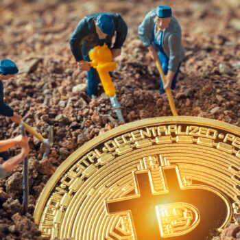 Four miniature figurines with tools appear to dig around a large, shiny gold Bitcoin coin partially buried in soil, symbolizing the concept of Bitcoin mining.