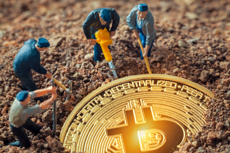 Four miniature figurines with tools appear to dig around a large, shiny gold Bitcoin coin partially buried in soil, symbolizing the concept of Bitcoin mining.