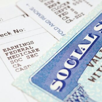 Close-up of a Social Security card placed on top of a pay stub, showing payroll details such as earnings, federal tax, Medicare, and Social Security deductions.