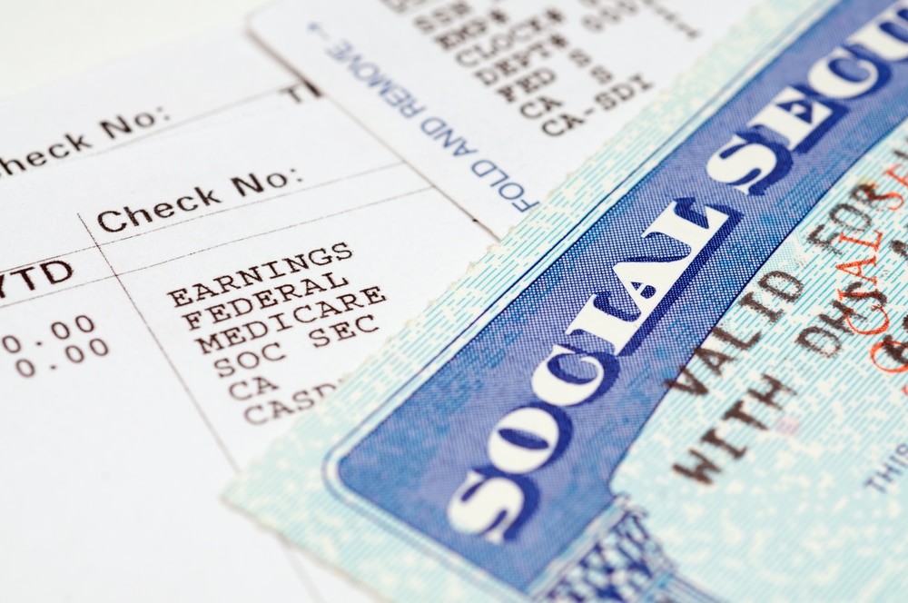 Close-up of a Social Security card placed on top of a pay stub, showing payroll details such as earnings, federal tax, Medicare, and Social Security deductions.