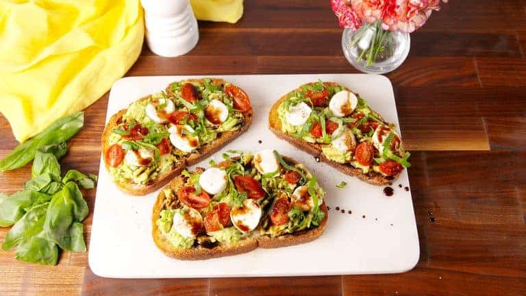 A person sitting at a round white table, writing in a notebook. There are books and a small plant on the table, and blue charts on the wall in a bright, minimalist room.