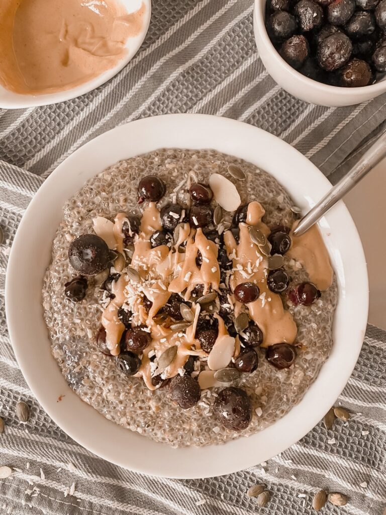 A clear glass vase with dried beige grasses sits beside two yellow books and a gold etc ornament on a white surface against a white background.