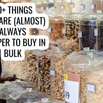 A person scoops mixed nuts from a bulk bin in a store. Several clear containers filled with various nuts and dried foods are visible. Overlaid text reads, 20+ Things That Are (Almost) Always Cheaper to Buy in Bulk.