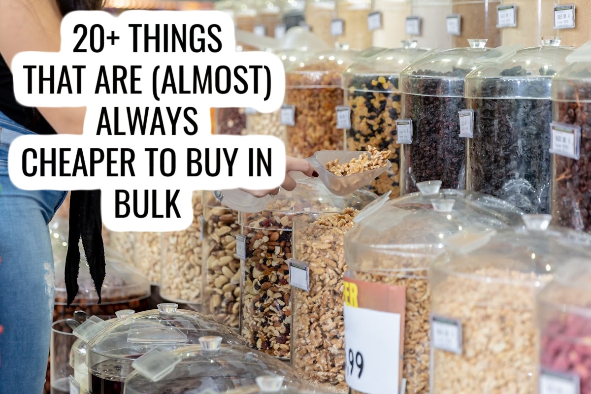 A person scoops mixed nuts from a bulk bin in a store. Several clear containers filled with various nuts and dried foods are visible. Overlaid text reads, 20+ Things That Are (Almost) Always Cheaper to Buy in Bulk.