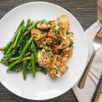 A delicious serving of sesame chicken with fresh green beans on a white plate, perfect for dinner.