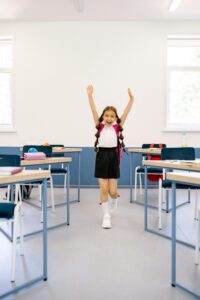 Happy girl with arms raised in a bright classroom, exuding positivity and excitement.