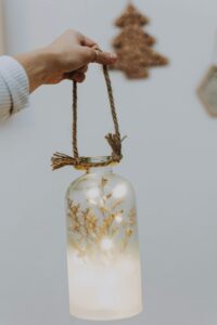 A handmade illuminated glass jar lantern with rustic rope handle indoors, ideal for cozy decor.