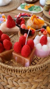 Handmade decorative candles adorned with fruity designs displayed in a woven basket.