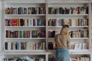 Blonde woman browsing a bookshelf in a library, conveying a love for reading and literature.