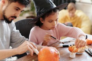 Father and daughter decorating pumpkins together for Halloween indoors.