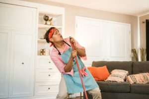 Cheerful man cleaning and singing into a broom at home, creating a fun atmosphere.