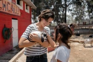 A joyful woman and girl interacting with a rabbit at a sunny outdoor petting zoo.