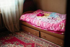 A warm and inviting bedroom scene featuring a floral pink bedspread, under-bed drawers, and a patterned rug.
