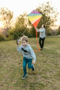 Father and son enjoying a sunny day flying a colorful kite together in a park.