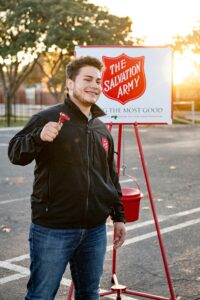 A cheerful volunteer ringing the Salvation Army bell outdoors during the day.