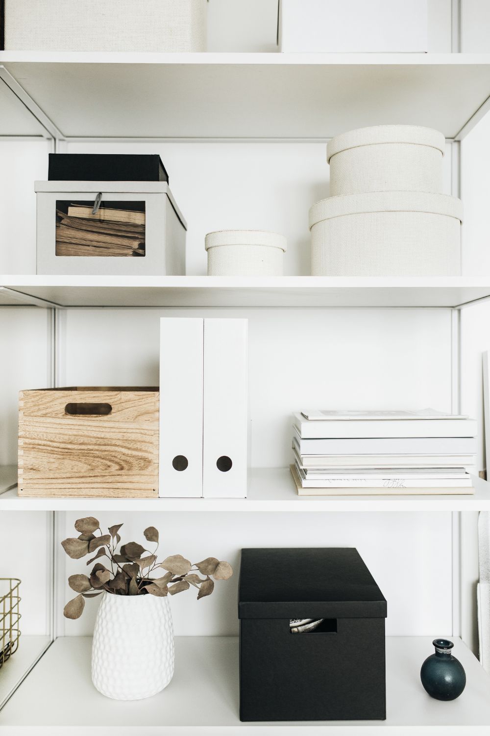 An organized office shelf with boxes, files and baskets in shades of black, white and neutral