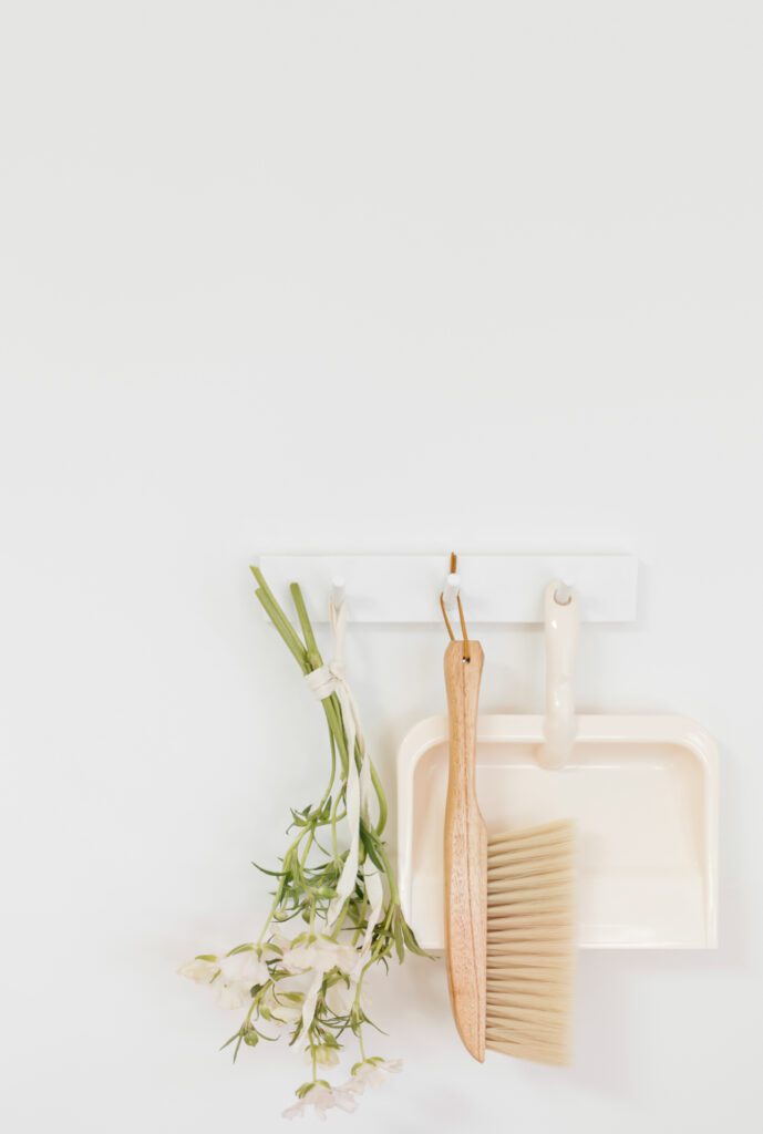 A neutral cleaning image, with a dustpan and wooden brush and a bundle of fresh Spring flowers for a Spring Cleaning checklist post.