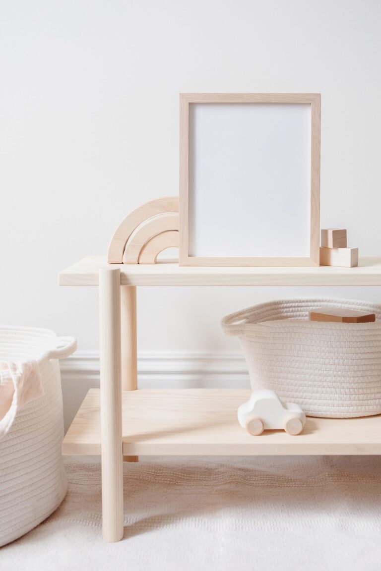A wooden shelf with a blank framed picture, wooden rainbow toy, two white woven baskets, and a white toy car in a minimal, neutral-toned room.
