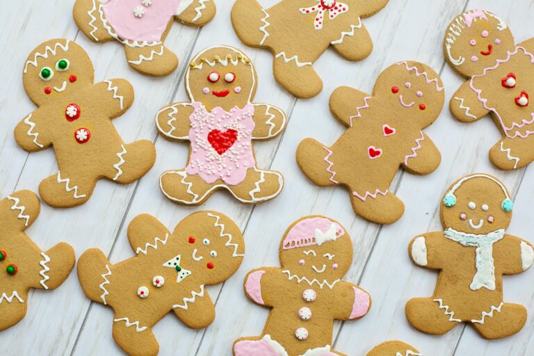 Decorated gingerbread cookies shaped like people are arranged on a white wooden surface, each with different icing designs, buttons, and facial expressions.