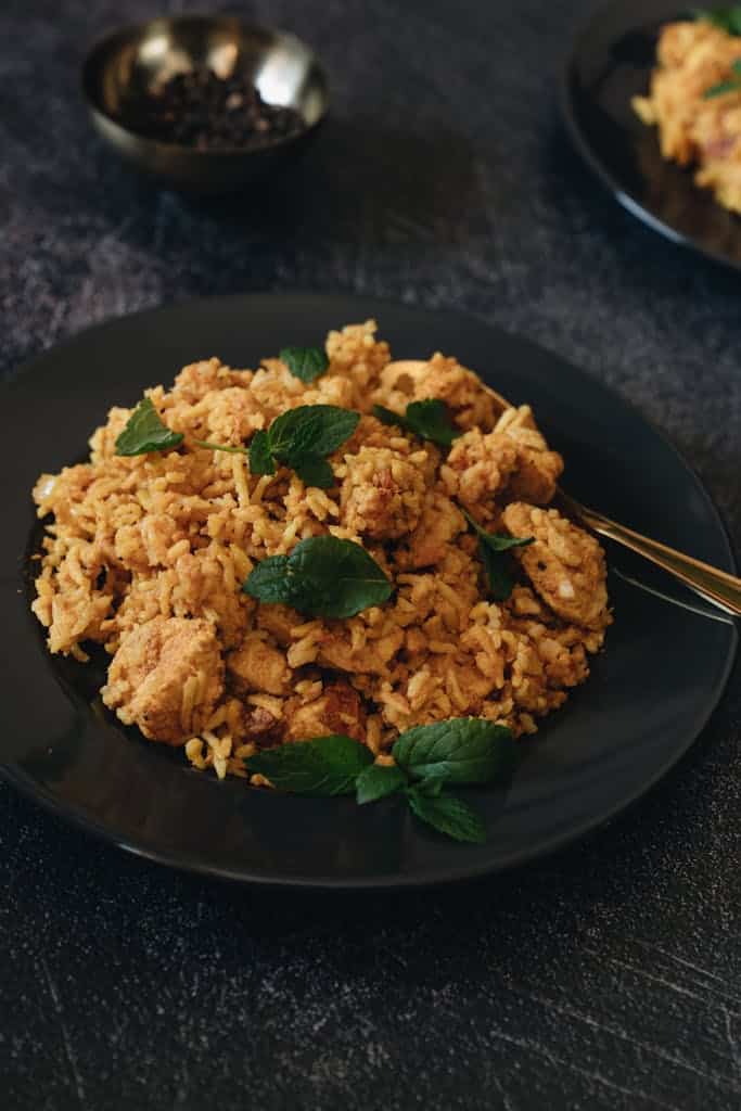 Appetizing chicken biryani garnished with mint on a black plate, perfect for dinner.