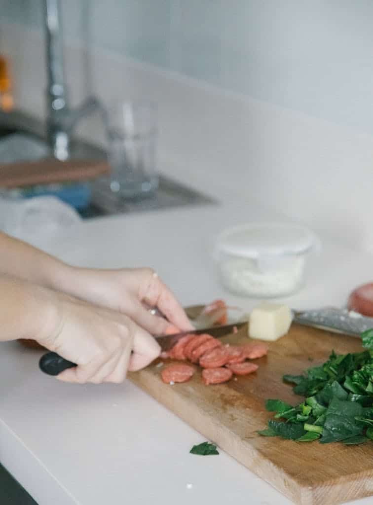 Hands slicing meat and vegetables for Turkish cuisine on a chopping board.