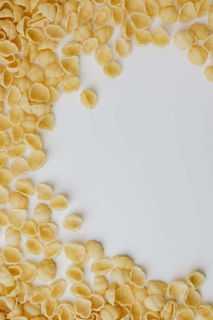 Overhead view of uncooked pasta shells scattered on a white surface.