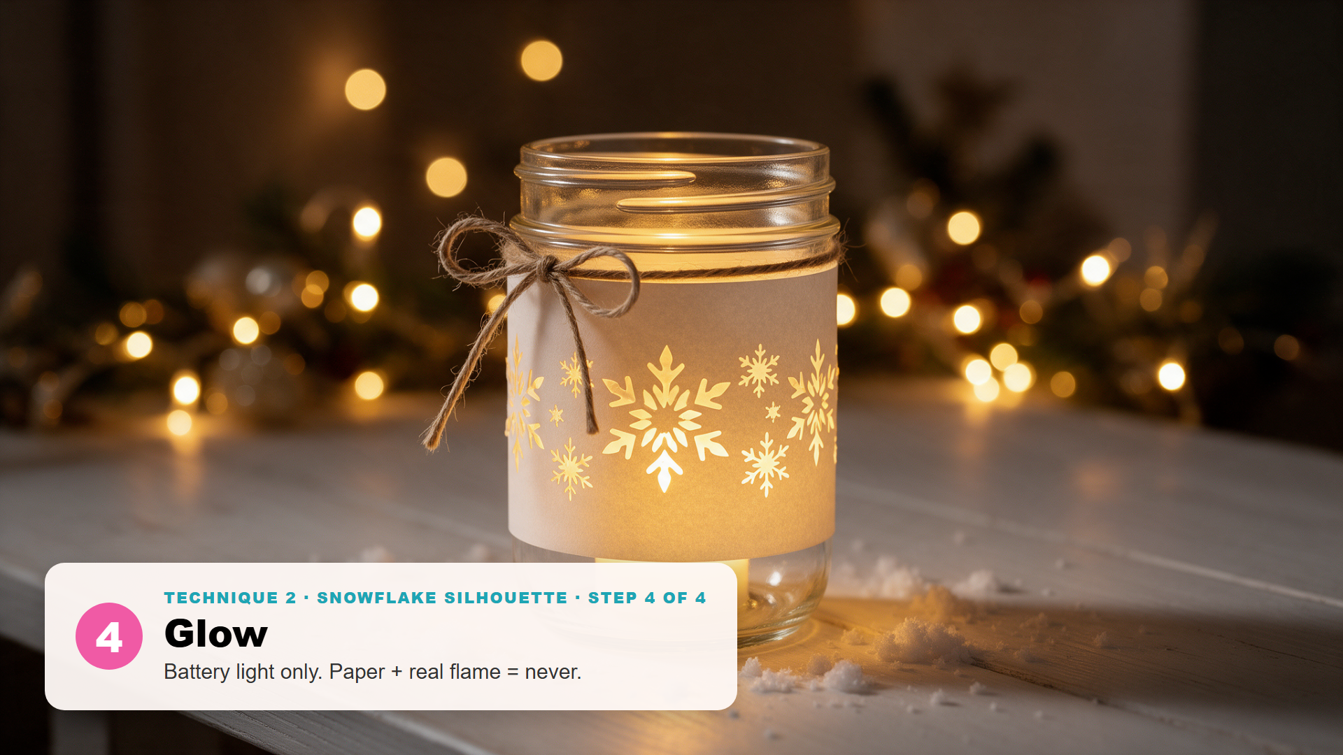Mason jar Christmas luminary wrapped in an ivory paper band with white snowflakes, tied with twine and glowing on a table at night